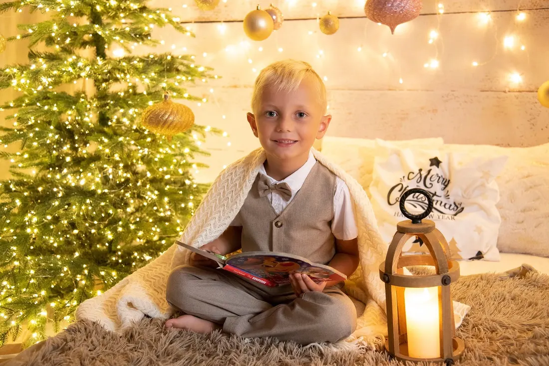 Chłopiec czyta książkę przy choince w ciepłym świetle lampionów