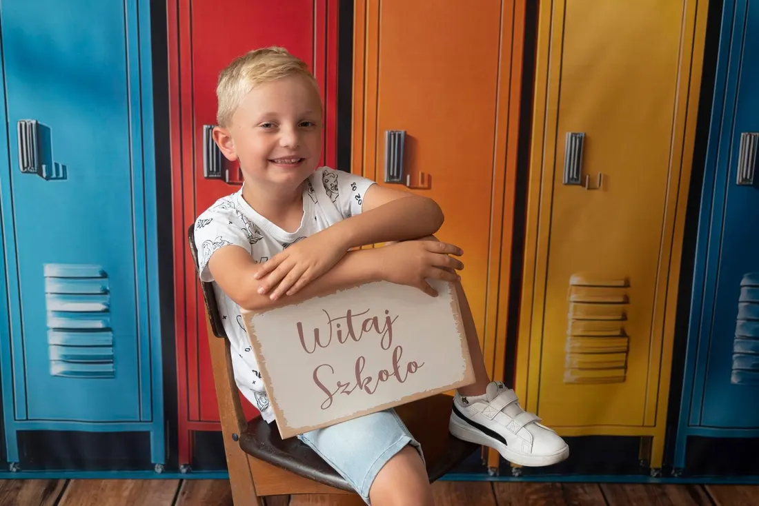 Uczeń z tabliczką Witaj szkoło na tle szafek