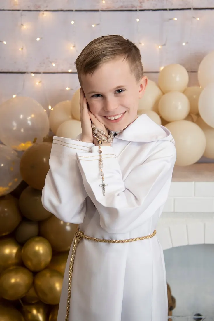 Chłopiec w albie komunijnej na tle złotych balonów