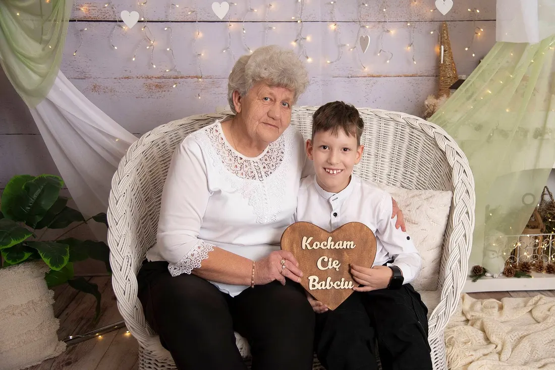 Babcia z wnukiem na białej wiklinowej sofie, trzymają drewniane serce